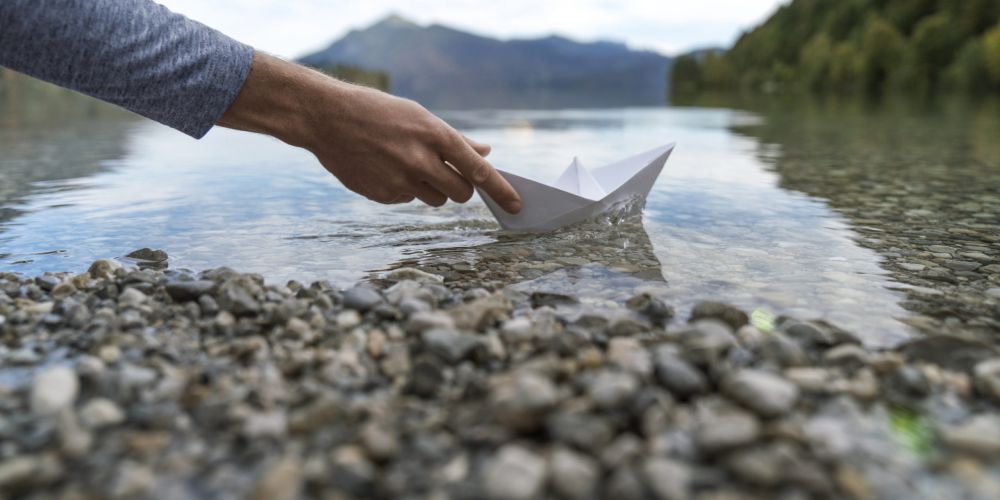Hand mit Papierboot im Flussbett