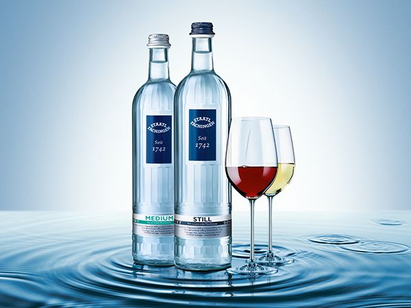 Zwei Wasserflaschen und Weingläser in Pfütze vor blauem Hintergrund