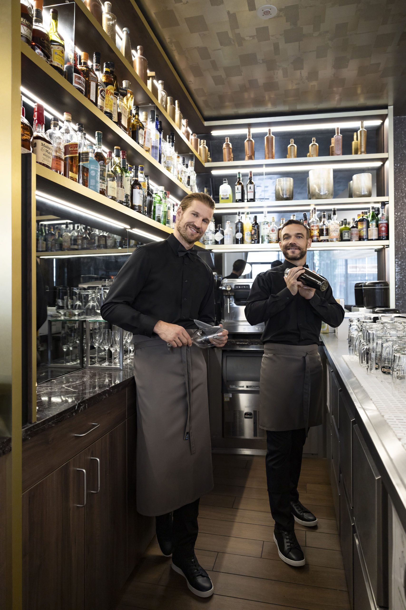 Zwei Herren mit Kochschürzen stehen hinter der Bar