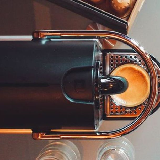Kaffee fließt aus Kapselmaschine in Kaffeeglas Vogelperspektive