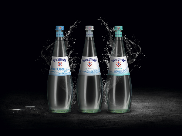 Drei Gerolsteiner Mineralswasserflaschen mit Wasserspritzern stehen vor schwarzem Hintergrund