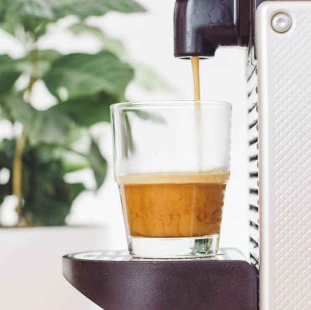 Kaffee aus Kapselmaschine fließt in Kaffeeglas