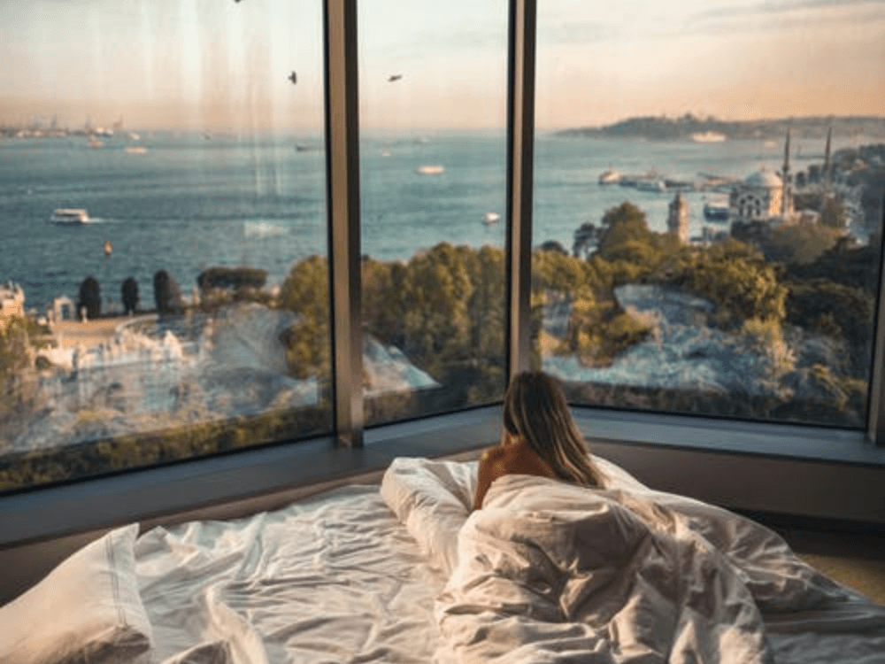 Hotelgast liegt im Bett und schaut aus dem Panoramafenster mit Blick auf das Meer