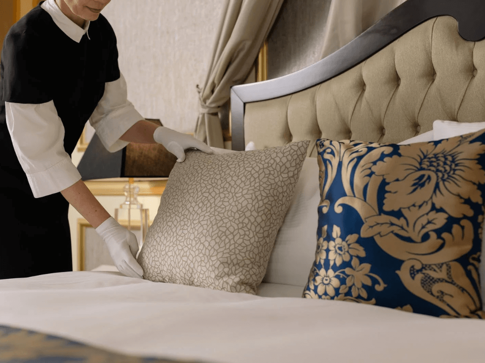 Zimmerfrau schüttelt Kissen eines Hotelbetts auf